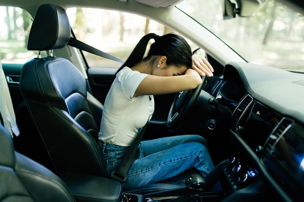 A tired girl, suffering from a headache and migraine, sits in the driver's seat of her vehicle, touching her painful forehead. She feels unwell and exhausted.