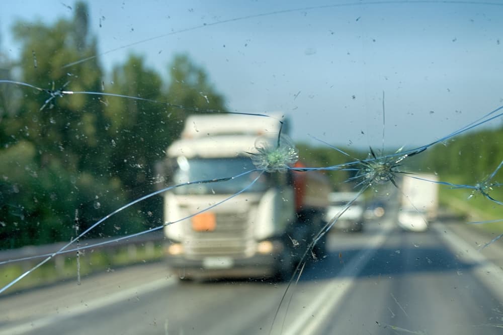 Highway through a broken windshield after encountering a truck with crushed stone.
