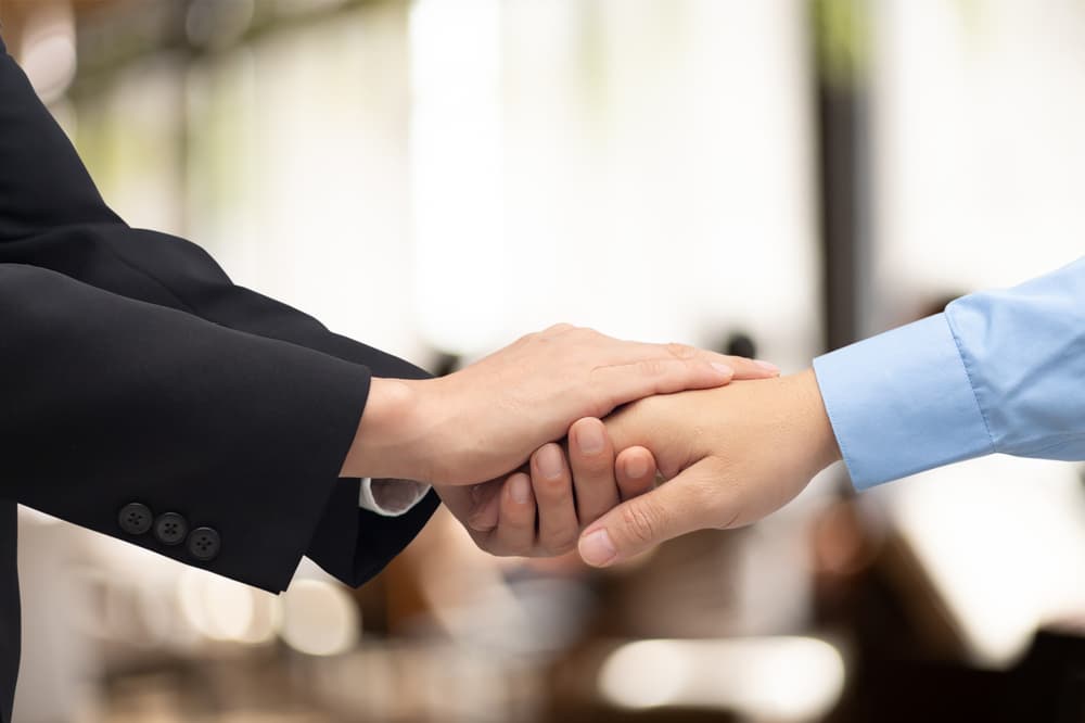 Two attorneys, in a gesture of partnership, shake hands in a law firm, symbolizing teamwork, mutual trust, honesty, and respect in their professional relationship.