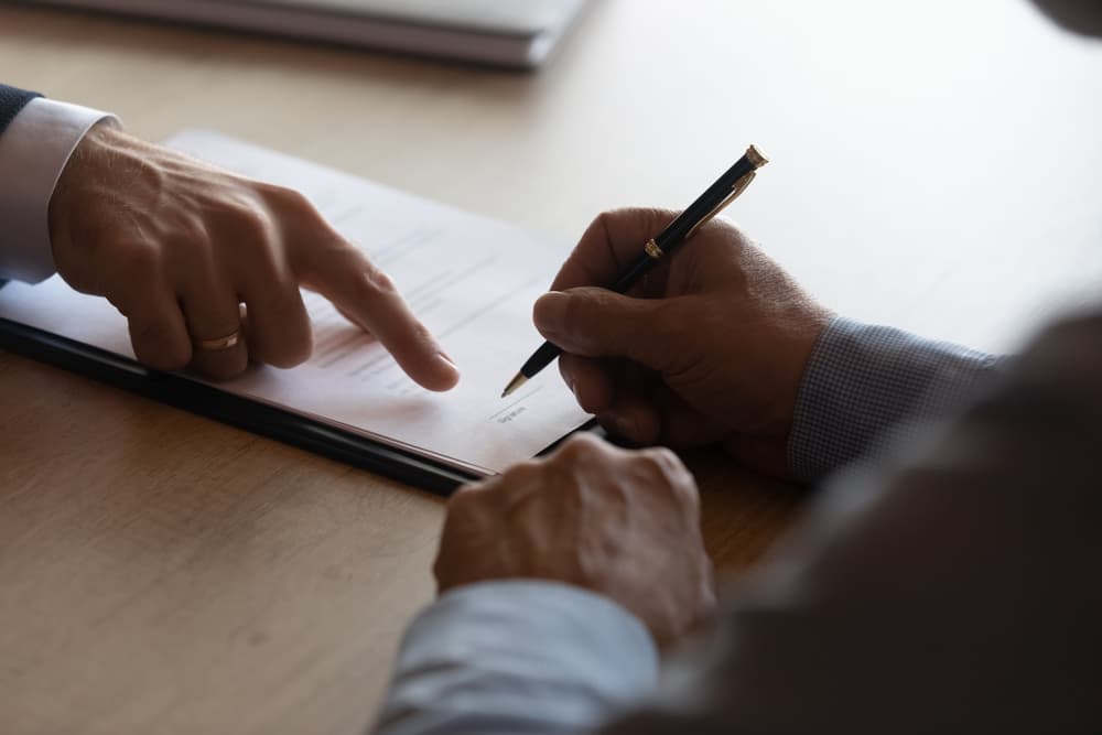 A close-up of two people reviewing and signing a document, with one pointing at the paper.