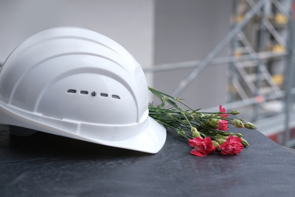 A white hard hat and a bouquet of red flowers placed on a dark surface.