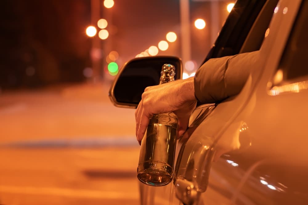 Drunk man driving a car with a bottle of beer at the night