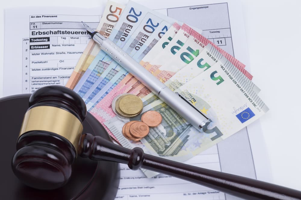 A gavel, Euro banknotes, coins, and a tax form on a desk with a pen.