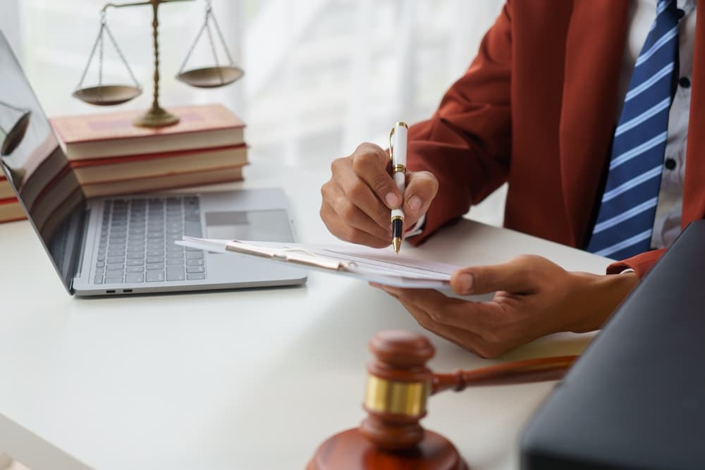 A lawyer reviewing documents at a desk with a laptop, gavel, and scales of justice.