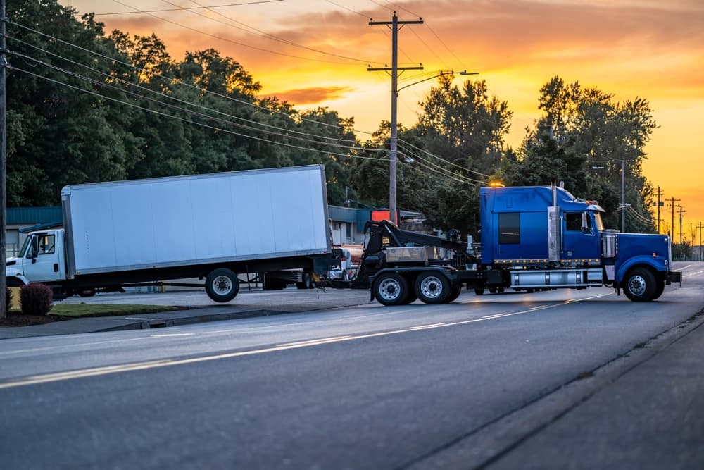 semi truck tractor towing broken after accident day cab semi truck with box trailer driving on the local road at evening time