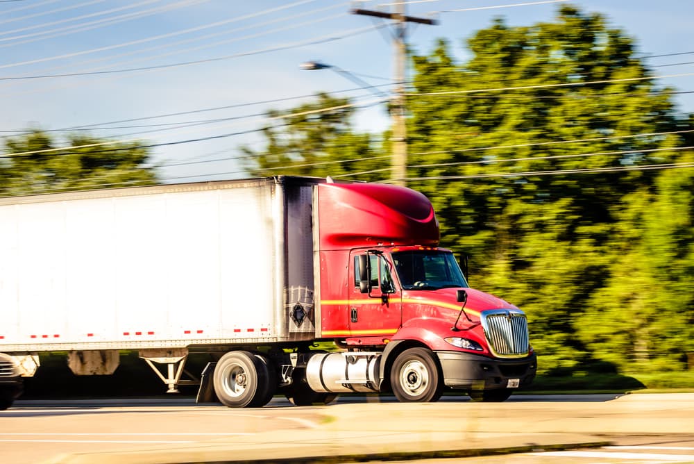 A red cargo truck is running down the highway captured early morning during summer season.