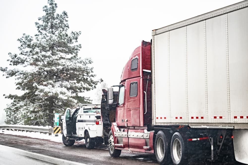 A red semi-truck and a service vehicle parked on the roadside after a trucking accident in snow.